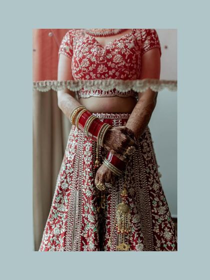 A detail shot of a bride's red lehenga, focusing on the intricate embroidery and her traditional red chooda bangles.