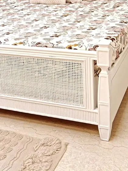 A detailed shot of the footboard on our white cane bed. You can see the combination of the woven cane panel and the classic turned-wood post, details that define its quality craftsmanship.