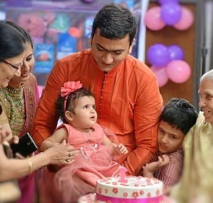A multi-generational moment around the birthday cake. The family gathers to watch the little girl, creating a heartwarming, candid photograph.
