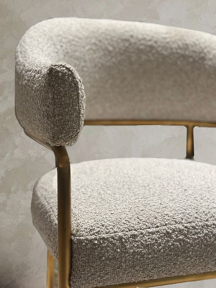 A detail shot of the custom bouclé chair, showing the texture of the fabric and the refined finish of the gold accented frame.