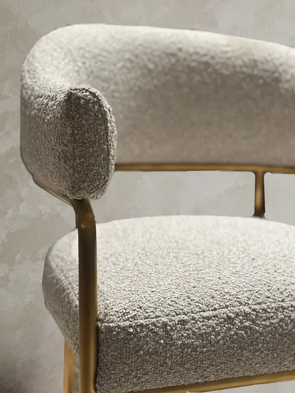 A detail shot of the custom bouclé chair, showing the texture of the fabric and the refined finish of the gold accented frame.
