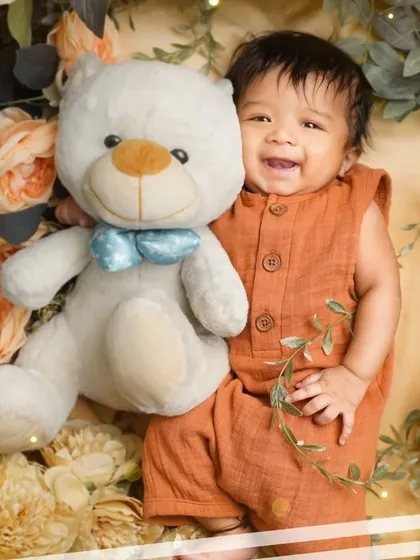 A happy three-month-old baby boy cuddling with his teddy bear. These milestone sessions are perfect for capturing their budding personality.