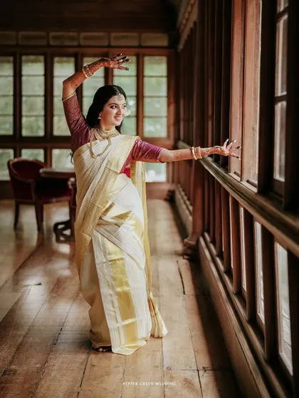 A graceful portrait of the bride in a dance-like pose, her kasavu saree flowing beautifully in the light of the corridor.
