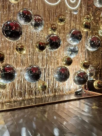 Celebrating 50 years of love with a touch of retro glam. This anniversary setup features a wall of shimmering gold fringe and dozens of silver and gold disco balls, creating a dazzling dance floor for the happy couple.