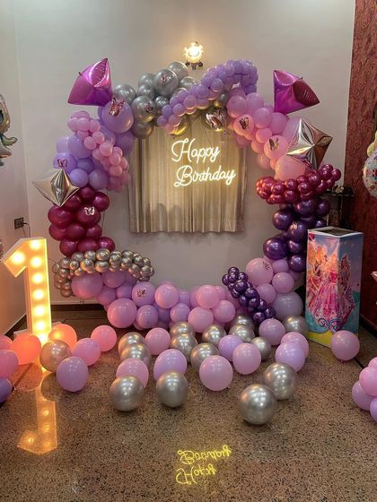 A princess-themed birthday party with a modern twist. This setup features a circular balloon arch in shades of pink and purple, a neon 'Happy Birthday' sign, and a light-up marquee number '1'.