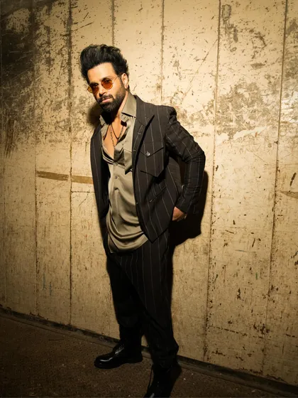 Rithvik Dhanjani wears a striped brown jacket in tropical wool, paired with a satin kurta. The look redefines formalwear by blending traditional Indian silhouettes with modern tailoring, featuring zip details and elbow patches.