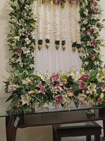 A beautiful floral frame for a Ganpati celebration, made with fresh pink and white lilies and hanging jasmine garlands.
