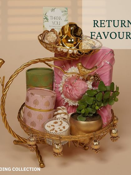 An elegant return favor arrangement on a golden two-tiered stand. It features beautifully packaged gifts, a small plant, and a thank you card for guests.