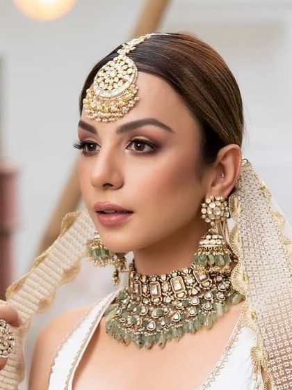 A stunning morning bride in a white and gold lehenga. The makeup is kept soft and dewy, with a focus on radiant skin.