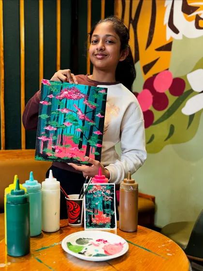 A young girl proudly displays her finished painting of a mystical forest. Each artist brings their own unique vision to the theme.