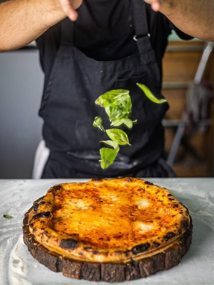 World-class pizzas and all. Another shot of basil leaves being added to a pizza, capturing the motion and the fresh ingredients.