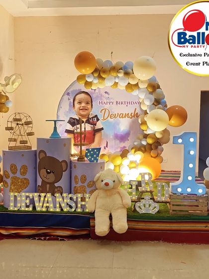 A sweet teddy bear-themed first birthday. The decor includes a personalized backdrop, a cute teddy bear prop, and a large light-up number '1'.