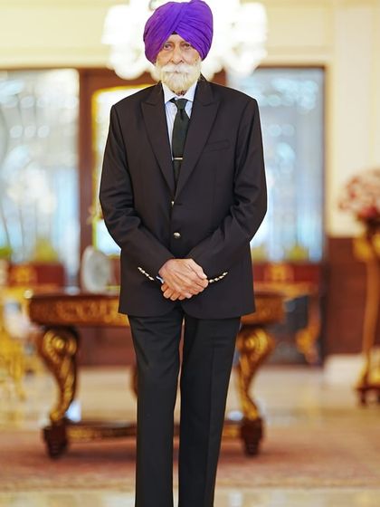His Highness Brigadier Sukhjit Singh in a full-length view of his classic black suit. The tailoring is clean and precise, designed to honour his dignified presence.