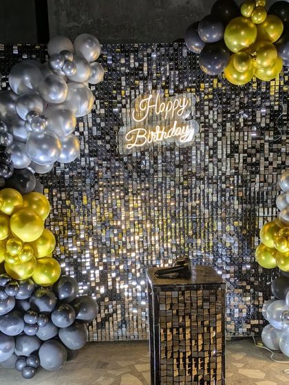 The black sequin backdrop setup with asymmetrical balloon clusters in gold, silver, and black for a modern, chic look.