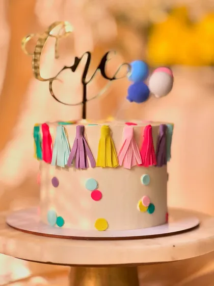 A festive and colorful cake for a first birthday party. This lemon-flavored cake is decorated with a fun tassel garland, confetti dots, and a balloon topper.