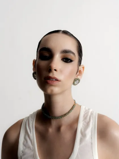 A direct and powerful portrait that gives a clear view of the intricate choker and earring set. The model's intense gaze adds to the strength of the image.