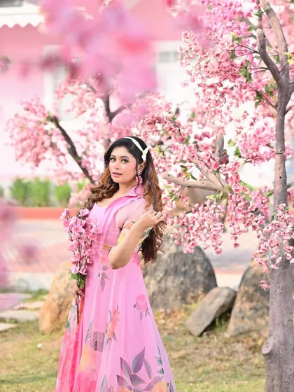 The model stands among the cherry blossom trees, creating a fully immersive and romantic fashion portrait.