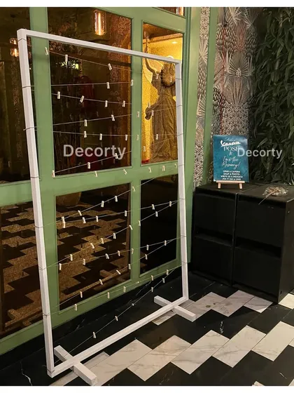 A simple and effective photo display frame with string lights and clips, ready for guests to hang instant photos at a corporate event.