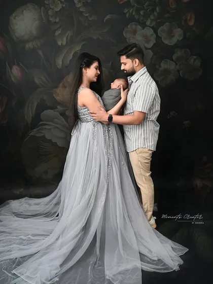 An elegant family portrait with their newborn. The mother's sparkling grey gown adds a touch of glamour to this classic photo against a dark floral backdrop.