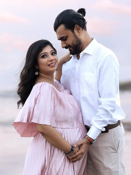 A romantic and candid shot of the couple sharing a look. The soft light of the evening sky creates a dreamy atmosphere for this beach maternity portrait.