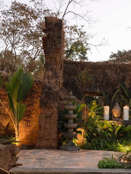 A tranquil corner at Sanctuary Bar, where a stone lamp, candles, and a Buddha head are nestled among lush plants and crumbling ruins. The landscape design creates a spiritual and serene atmosphere.
