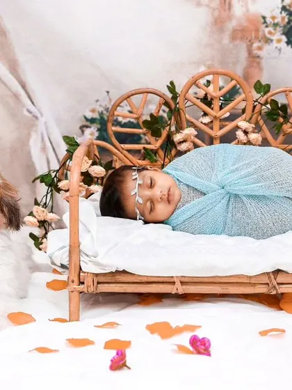 A full scene showing a baby sleeping in a miniature rattan bed while their loyal dog sits guard. The bohemian setup with flowers and a teepee adds a whimsical touch.