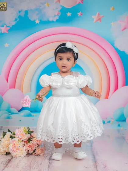 A dreamy first birthday setup with a pastel rainbow and clouds. This little angel looks perfect in her white dress.