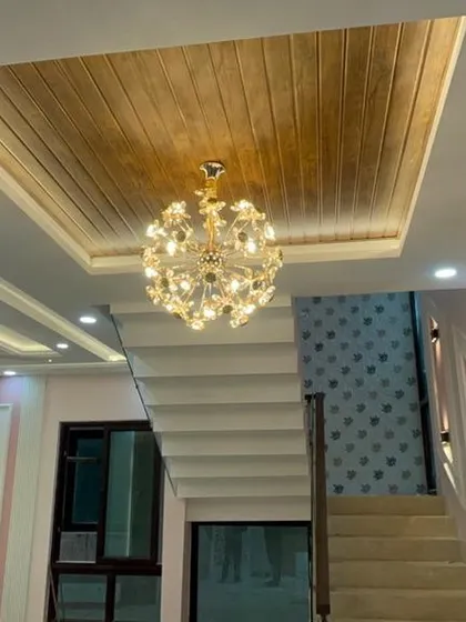 Our expertise in false ceilings and lighting can transform any room. This intricate design with a wooden panel and a grand crystal chandelier adds a layer of sophistication and warmth to the living space.