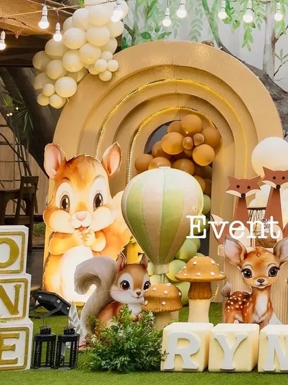 A close-up of Ryne's woodland decor, highlighting the adorable squirrel and deer cutouts. The setup includes "ONE" blocks and a soft, earthy color palette with layered arches creating depth.