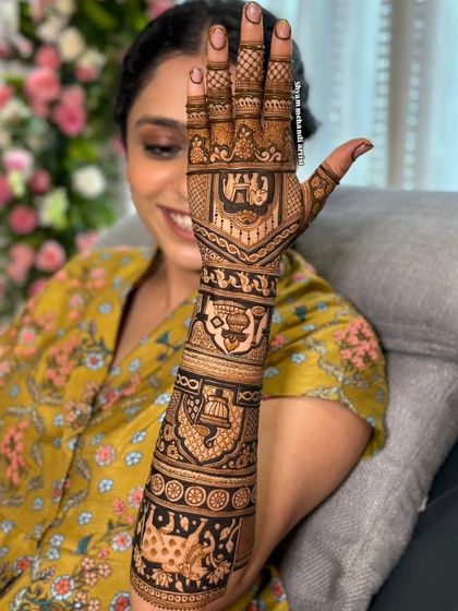 A bride showcasing her full-arm mehandi, which features traditional symbols like the kalash (pot) and elephants.