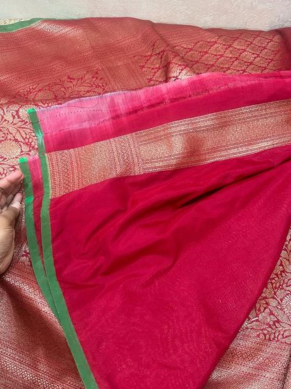 The plain pink blouse piece with a simple green and gold border, a perfect match for its corresponding Banarasi silk saree.