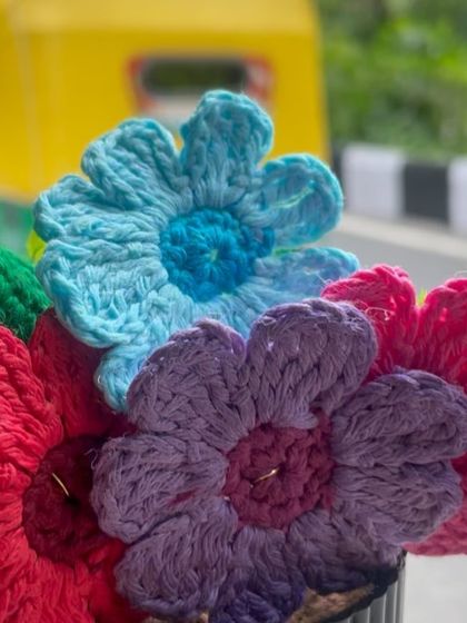 A close-up of the vibrant, multi-colored crochet flowers. You can see the different shades of red, purple, and blue, each stitched to create a full and cheerful bouquet.