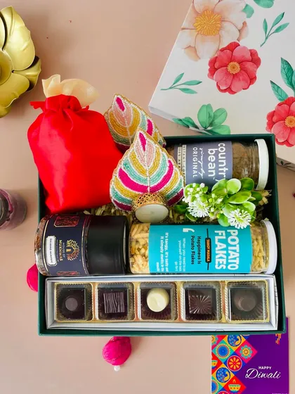 This floral box hamper is packed with a variety of treats. It includes premium chocolates, snacks, coffee, and colorful beaded T-light holders.