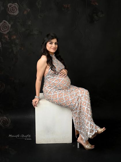 A glamorous seated portrait. The mom-to-be exudes confidence and style in this full-length shot, showing off the stunning silver-beaded gown.