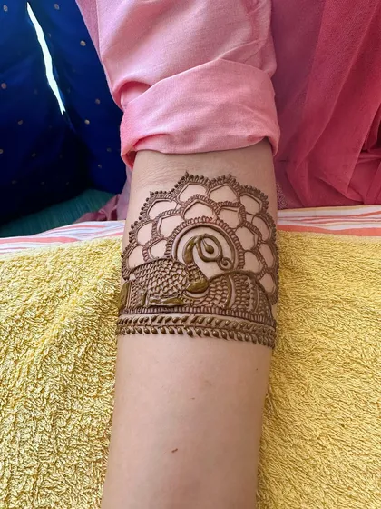 A close-up of a peacock armband, showcasing the fine lines and detailed feather patterns that I carefully create with a steady hand.