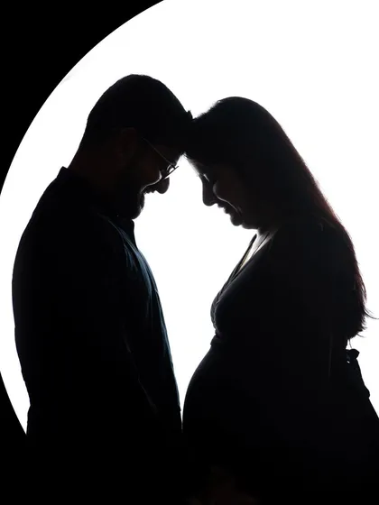 An intimate silhouette portrait of an expecting couple, their foreheads touching in a moment of quiet connection. This artistic maternity photo uses backlighting to create a beautiful, high-contrast image that focuses on their bond and the shape of the baby bump.