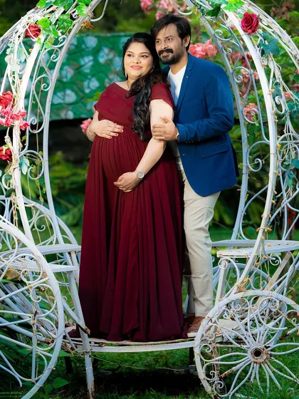 A romantic portrait of an expecting couple in a Cinderella-style carriage. The rich color of the maternity gown stands out beautifully against the white, ornate prop.