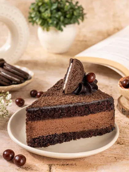 A slice of rich chocolate Oreo mousse cake. The styling with a book in the background creates a cozy, relaxing vibe, perfect for a quiet moment of indulgence.