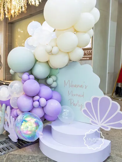 A welcome stand for Mihana's mermaid party, decorated with pastel purple and green balloons, clear bubble balloons, and seashell cutouts.