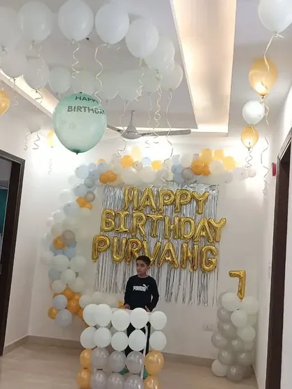 A first birthday celebration for Purvang at home. We created a backdrop with a silver shimmer curtain and a balloon arch in white, grey, and yellow, with balloons on the ceiling to complete the festive look.
