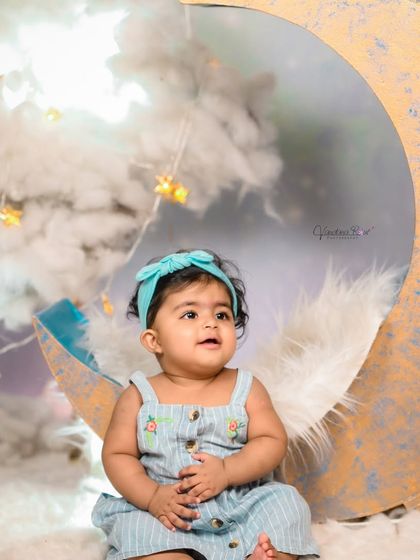 A close-up of a baby on the moon prop, showing the detailed texture of the moon and the soft, fluffy feather boa accent.