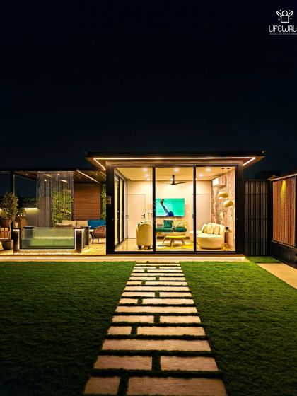 A wide shot of a completed project, showing the glass house, the glass-walled pool, and the stone pathway leading through the artificial grass lawn.