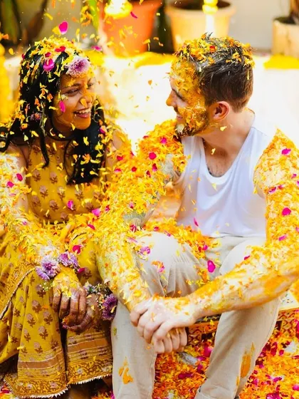 I love planning a 'phoolon ki holi' for the Haldi ceremony. This candid shot captures the pure, uninhibited joy of a couple surrounded by their loved ones, covered in turmeric and a rainbow of flower petals.
