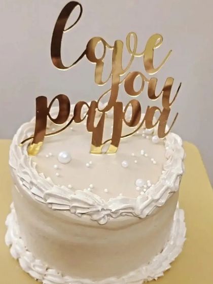 An elegant white cake with a beautiful gold "Love you Papa" topper for Father's Day.
