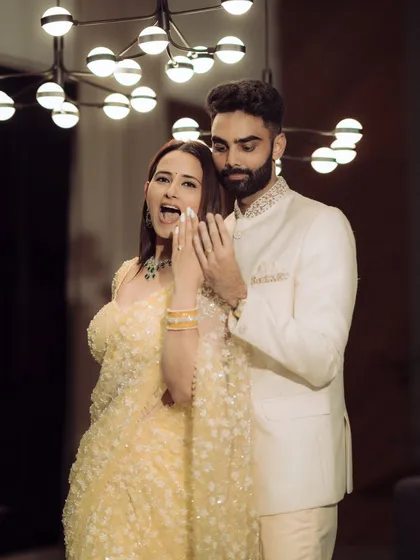 A playful moment showing off the new engagement ring. The excitement and joy are palpable in this candid shot, beautifully lit by a modern chandelier, adding a touch of glamour to the celebration.