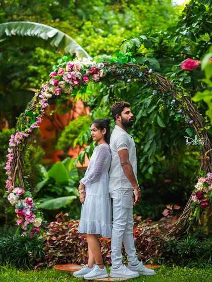 A couple stands back-to-back in front of a rustic floral arch, a creative and stylish pose.