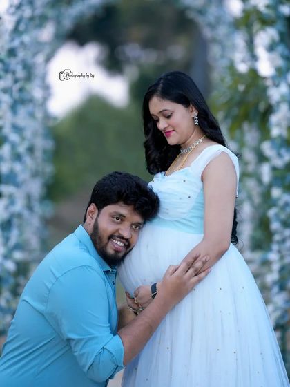 A heartwarming pose where the father-to-be listens to the baby bump. This shot, taken under our white floral arch, is a favorite for capturing the couple's connection.