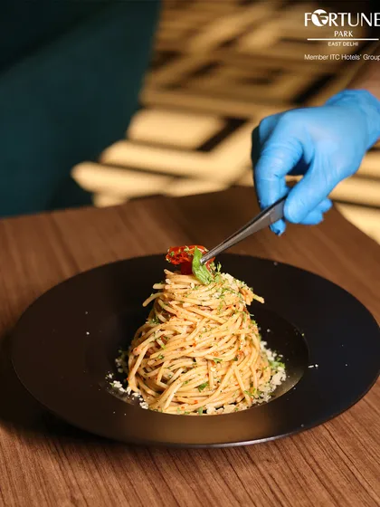 The final touch. A chef carefully garnishes a plate of spaghetti, ensuring it looks as good as it tastes.