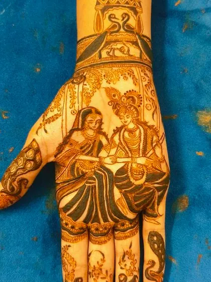 A beautiful portrait of Radha and Krishna sitting together, applied on a client's hand. The fine details bring the divine figures to life.