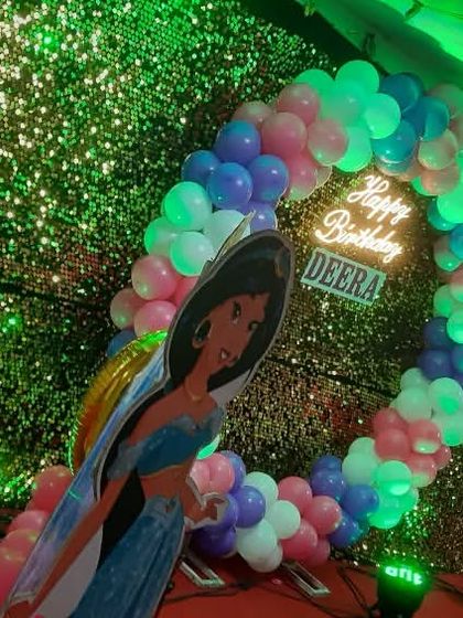 A Disney princess theme for a birthday party, featuring a Jasmine cutout against a sequin backdrop. The circular balloon arch with a "Happy Birthday" neon sign adds a magical touch.